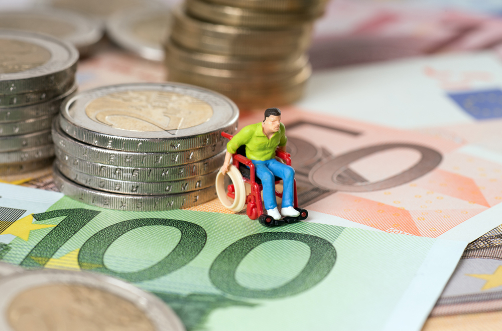 A small figurine of a person in a wheelchair, on top of a pile of banknotes and coins.