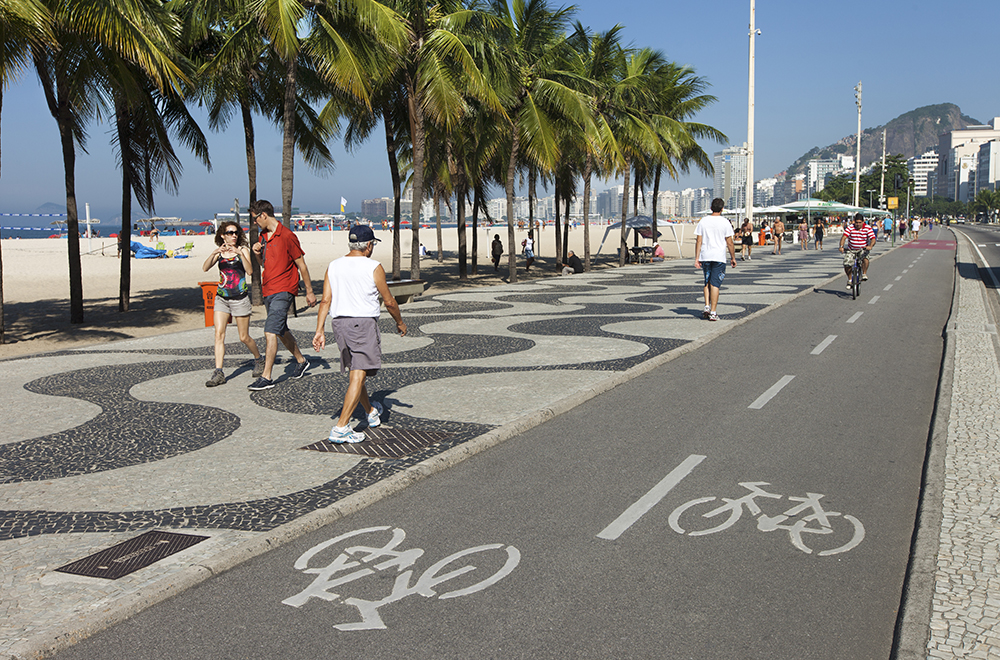 Rio de Janeiro, Brazil - June 2nd, 2013: One man drives a bicycle in the bike path located between Copacabana Beach famous sidewalk and Atlantica Ave. People walk in the sidewalk.