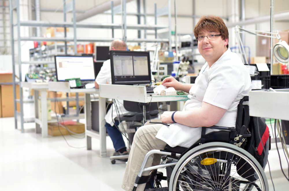 handicapped worker in a wheelchair assembling electronic components in a modern factory at the workplace