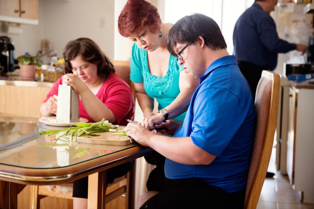 Couple in love of 26 years old Down Syndrome at her apartment in Montreal. They are learning to live in an apartment independently. They are cooking together.  the young men cutting vegetables. The mother in law show him how to do.
Color and horizontal photo was taken in Quebec Canada.