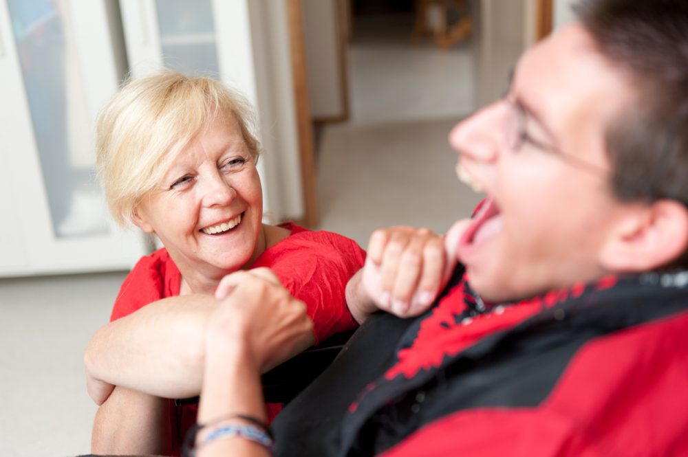 A female support worker dressed in red smiles at a male client, also dressed in red and smiling.