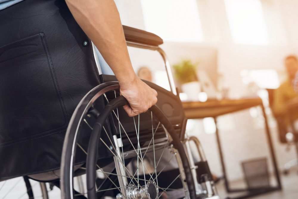 We see a wheelchair up close from the side. We can see a person's hand holding the wheel. The foreground is glowing like a sunset.