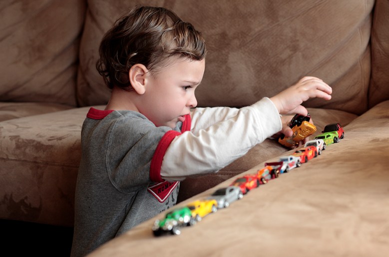 A young boy with brown hair, in a long sleeved shirt, lining up colourful cars on a table.