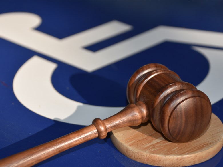 A disabled sign with a white symbol of a person in a wheelchair, underneath a wooden gavel.