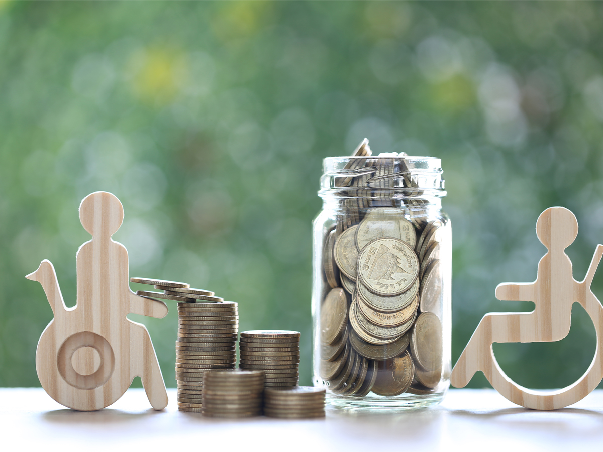 Wooden-look cutout figures of people in wheelchairs next to a pile of coins and a jar filled with money.
