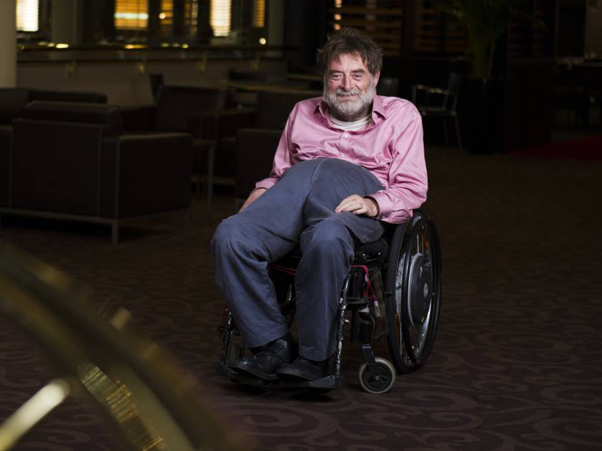 Dougie Herd, an older man in a wheelchair, wearing a pink shirt and navy blue pants.