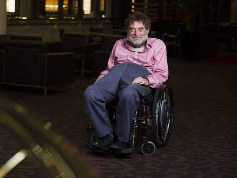 Dougie Herd, an older man in a wheelchair, wearing a pink shirt and navy blue pants.