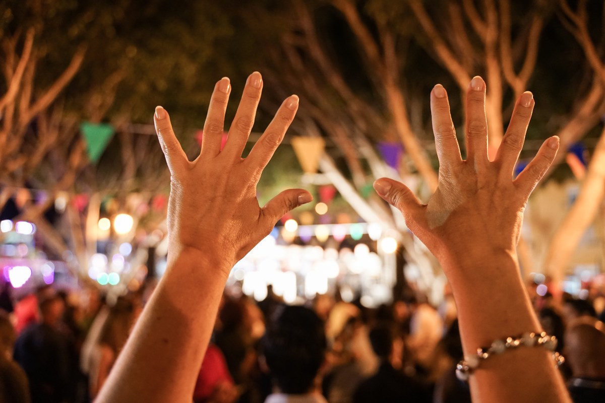 A person's hands up in the air in the foreground of what looks like a large party or event.