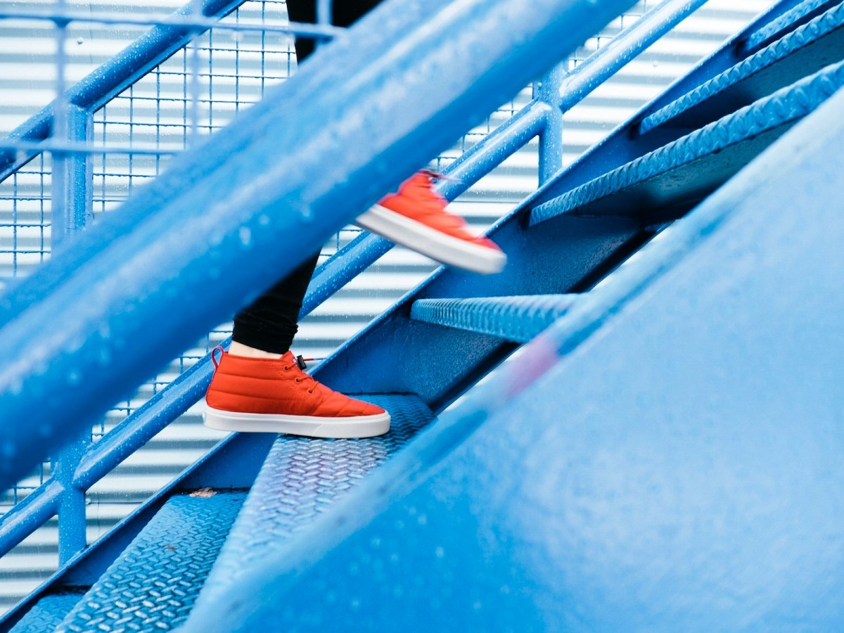 A set of metal stairs in blue, with orange runners climbing up them.