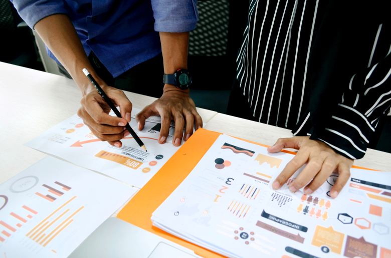 Two people are looking at sheets of paper covered in graphs and data. We can only see their arms and hands.