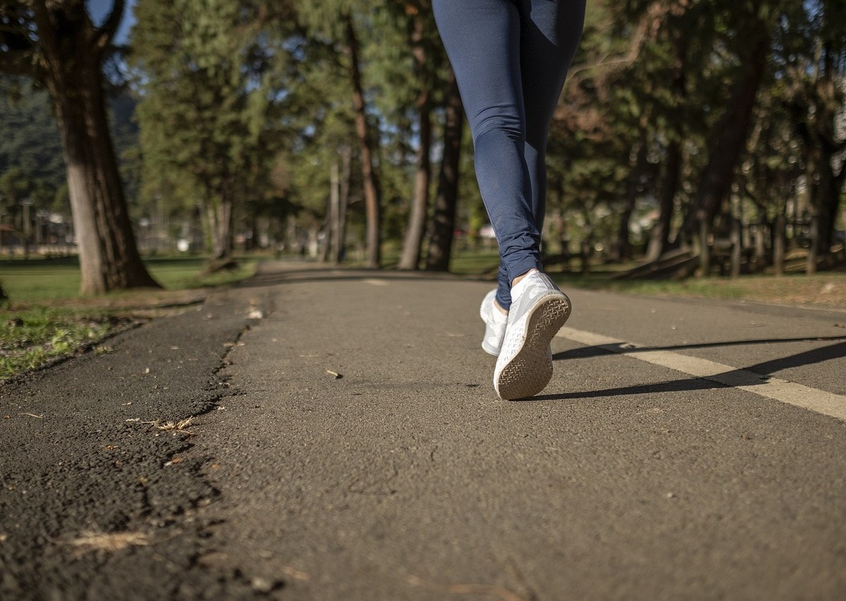 We see a foot in a white runner and blue leggings mid-stride, jogging through a park with trees.