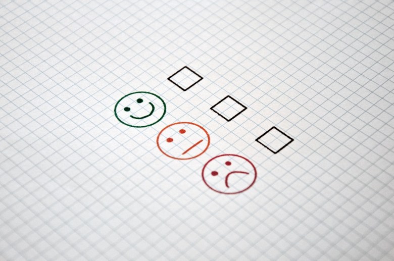 A checklist of three boxes on a piece of paper with a smiley face, neutral face and unhappy face next to the boxes.