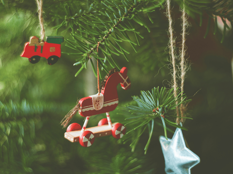 Baubles on a Christmas tree, including a red rocking horse, red truck and blue star. They are close up.
