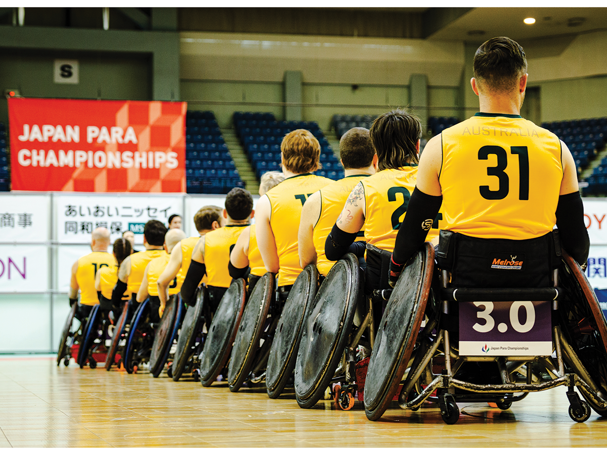 Athletes in wheelchairs in yellow jerseys in a stadium. We see them lined up from behind.