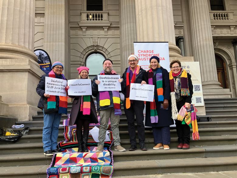 a goup of people on a flight of stone steps outside a stone old building. They are wearing corheted cloaks and holding protest signs.
