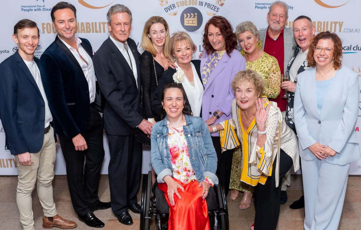 A group of people, men and women, some with visible disabilities and all dressed up nicely, stand together smiling excitedly at last year's Focus on Ability Film Festival.