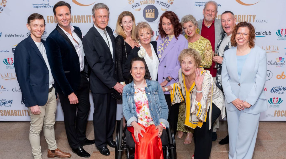 A group of people, men and women, some with visible disabilities and all dressed up nicely, stand together smiling excitedly at last year's Focus on Ability Film Festival.