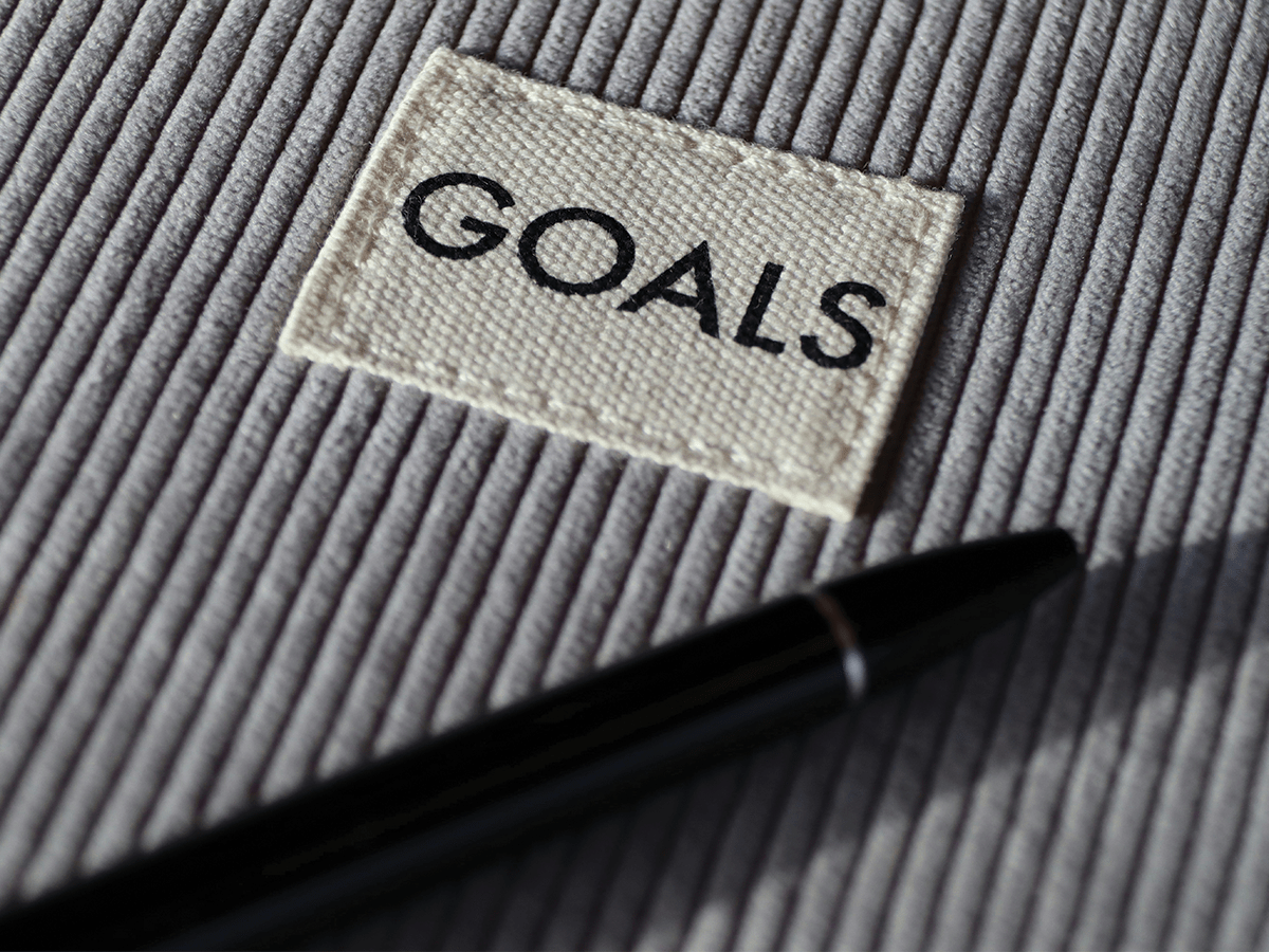 A grey striped, corduroy background with a small white tag that says GOALS, and a black pen underneath.