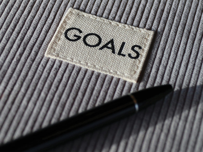A grey striped, corduroy background with a small white tag that says GOALS, and a black pen underneath.