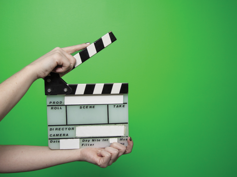 Two arms stretching out from the side of the screen holding a black and white movie clipper. It's against a green background.