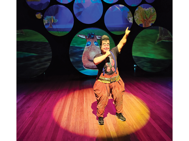 A man with Down syndrome performs in a costume in a spotlight on stage.