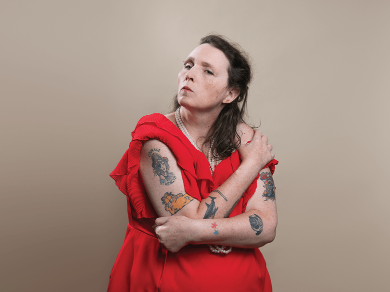 Artist Sarah Walker, a woman with dark hair in a red dress, with colourful tattoos on her arms.
