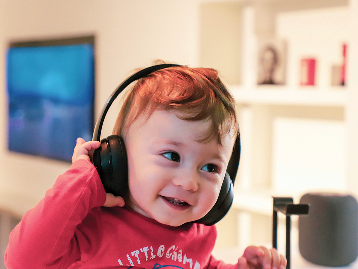A young boy in a red top smiles with headphones on.