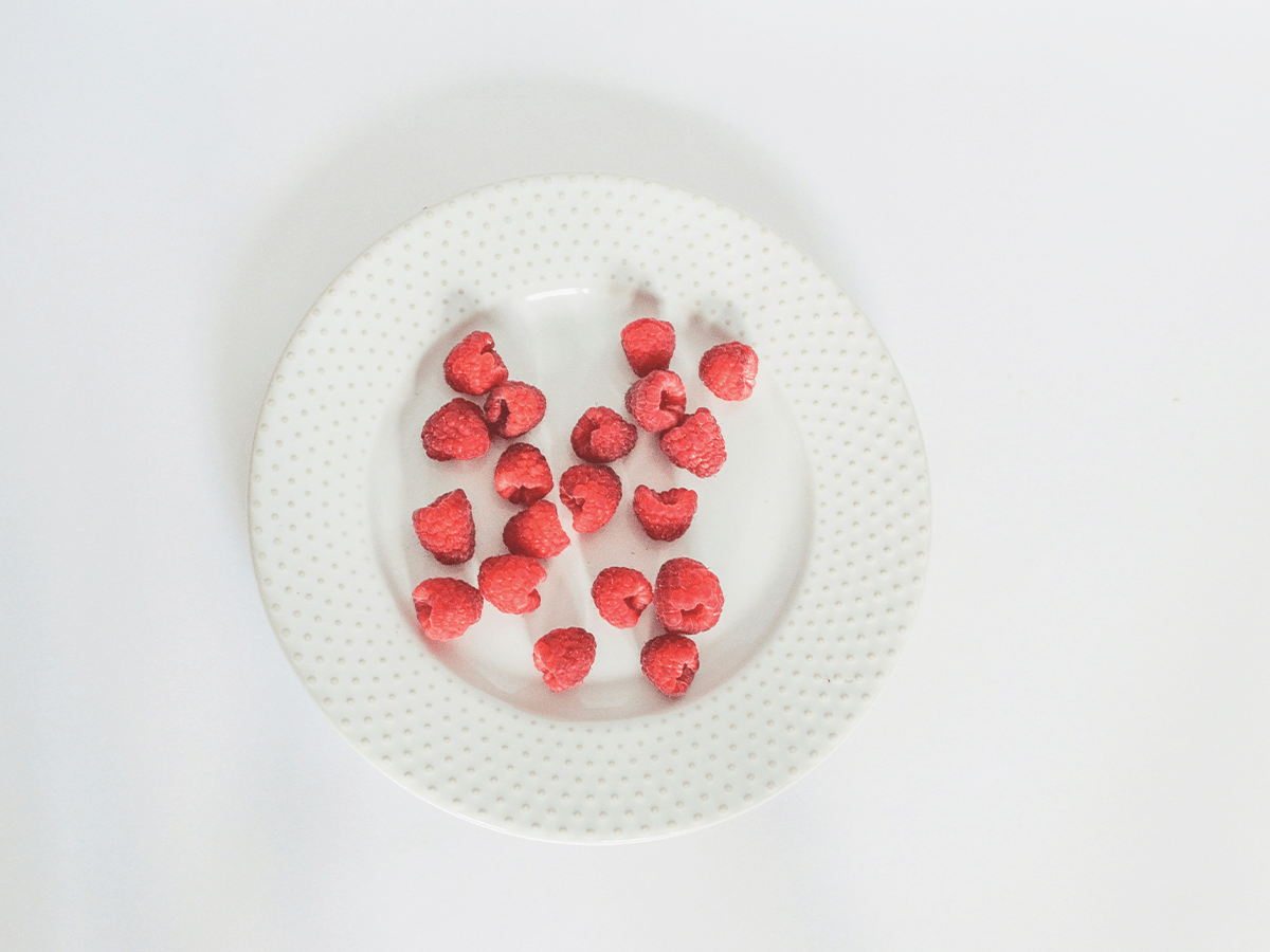 A white textured plate with red raspberries on it.