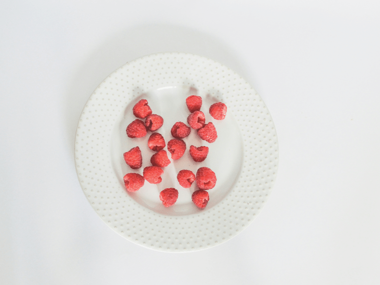 A white textured plate with red raspberries on it.